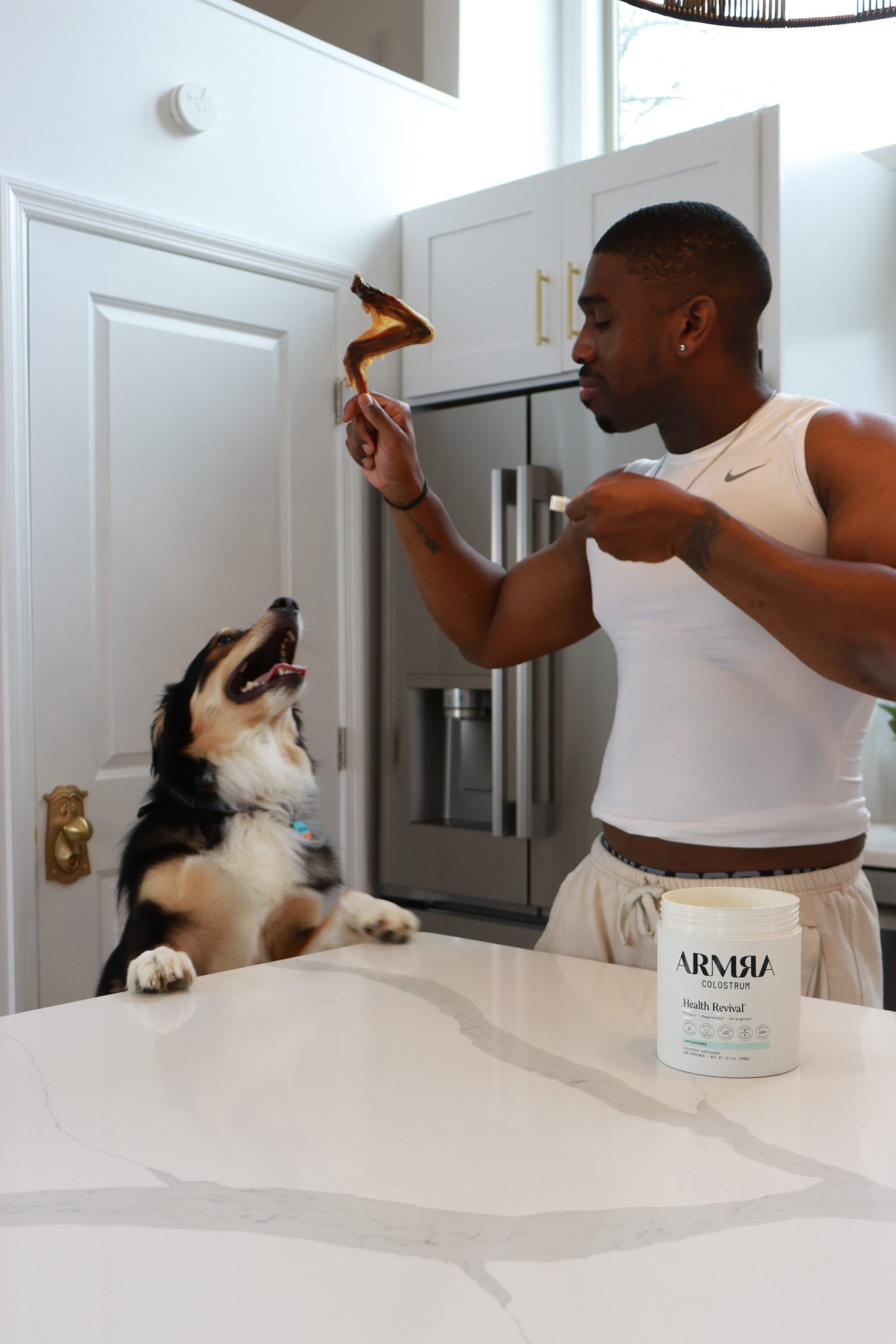Owner offering a duck wing to an Aussie shepherd in the kitchen